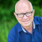 Robert Betz in blauem Hemd, Brille, unscharfer grüner Hintergrund