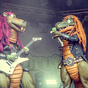 zwei Dinosaurier mit bunten Haaren haben Gitarre und Mikrofon dabei, sehen sehr rockig aus, auf der Bühne