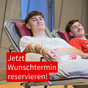 Das Bild zeigt eine Aufnahme zwei junger Erwachsener, die auf jeweils einer Liege liegen und Blut abgenommen bekommen. Die lachen in die Kamera. In der linken Ecke ist ein rot hinterlegter Schriftzug "Jetzt Wunschtermin reservieren!" zu lesen.