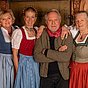 Harald Krassnitzer mit dem Garmischer Dreigesang in Tracht, gemeinsam lächelnd vor einer Holztür.