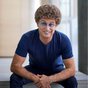 Atze Schröder sitzt mit Brille und blauem T-Shirt nach vorne gebeugt.