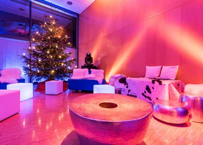 Stimmungsbild im Saal Rosenheim mit Loungemöbeln im KU'KO mit Weihnachtsbaum. Farbige Strahler.
