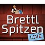 Logo der Sendung „Brettl Spitzen LIVE“ mit einem Musiker hinter einem hölzernen Bühnenpult und großer weißer Schrift auf rotem Hintergrund, ergänzt durch ein blaues Schild mit dem Wort „LIVE“.