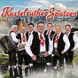 Die Kastelruther Spatzen in Tracht vor einer Alpenkulisse, ein Musiker mit Akkordeon, Gruppenfoto mit rotem Schriftzug.